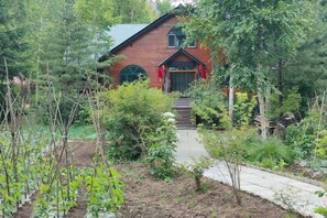 En byggnad med röda tegelväggar, en grön dörr och en liten veranda. En gång leder fram till dörren.