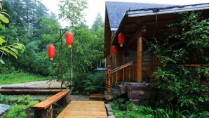A wooden cabin with a wooden deck leading to a porch, surrounded by lush greenery. - Senlinyu Villa (Fenglin County)
