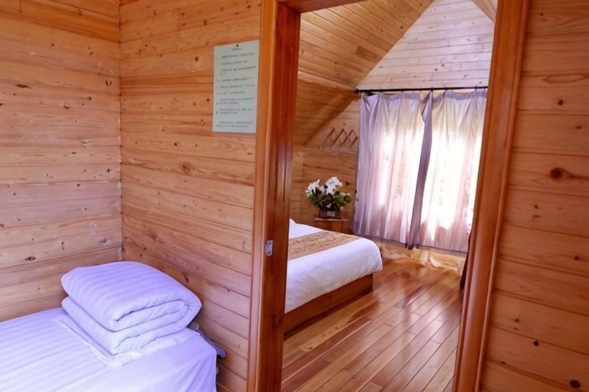 Una habitación de cabaña de madera con una cama, una mesita con una planta y una ventana con cortinas.