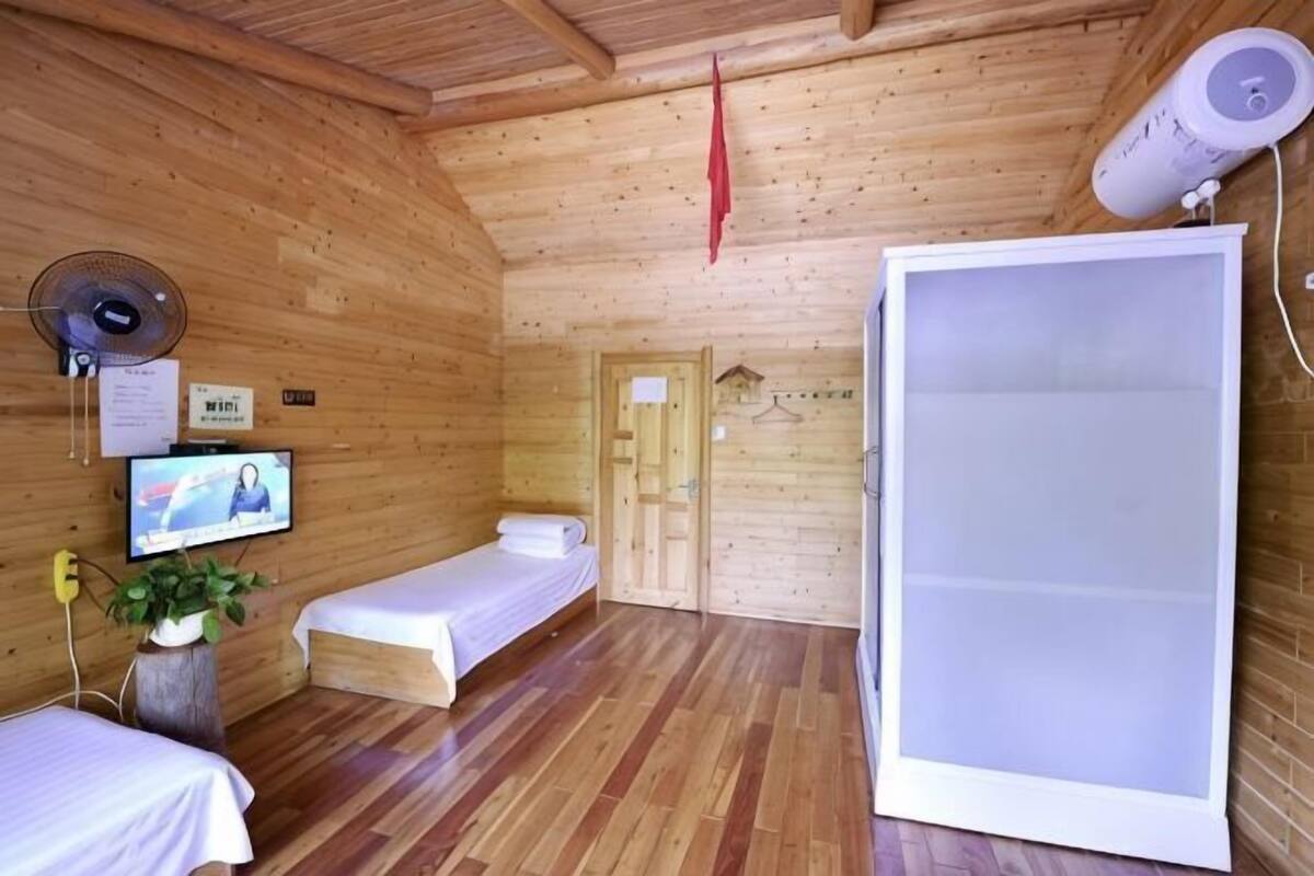 Una habitación de cabaña de madera con una cama, televisión, ventilador y un ventanal grande.
