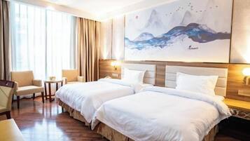 A hotel room with two beds, a sitting area with a chair and a small table, and a large painting of mountains on the wall.