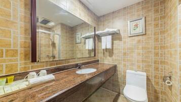 A bathroom with a marble sink, a toilet, a mirror, and tiled walls.