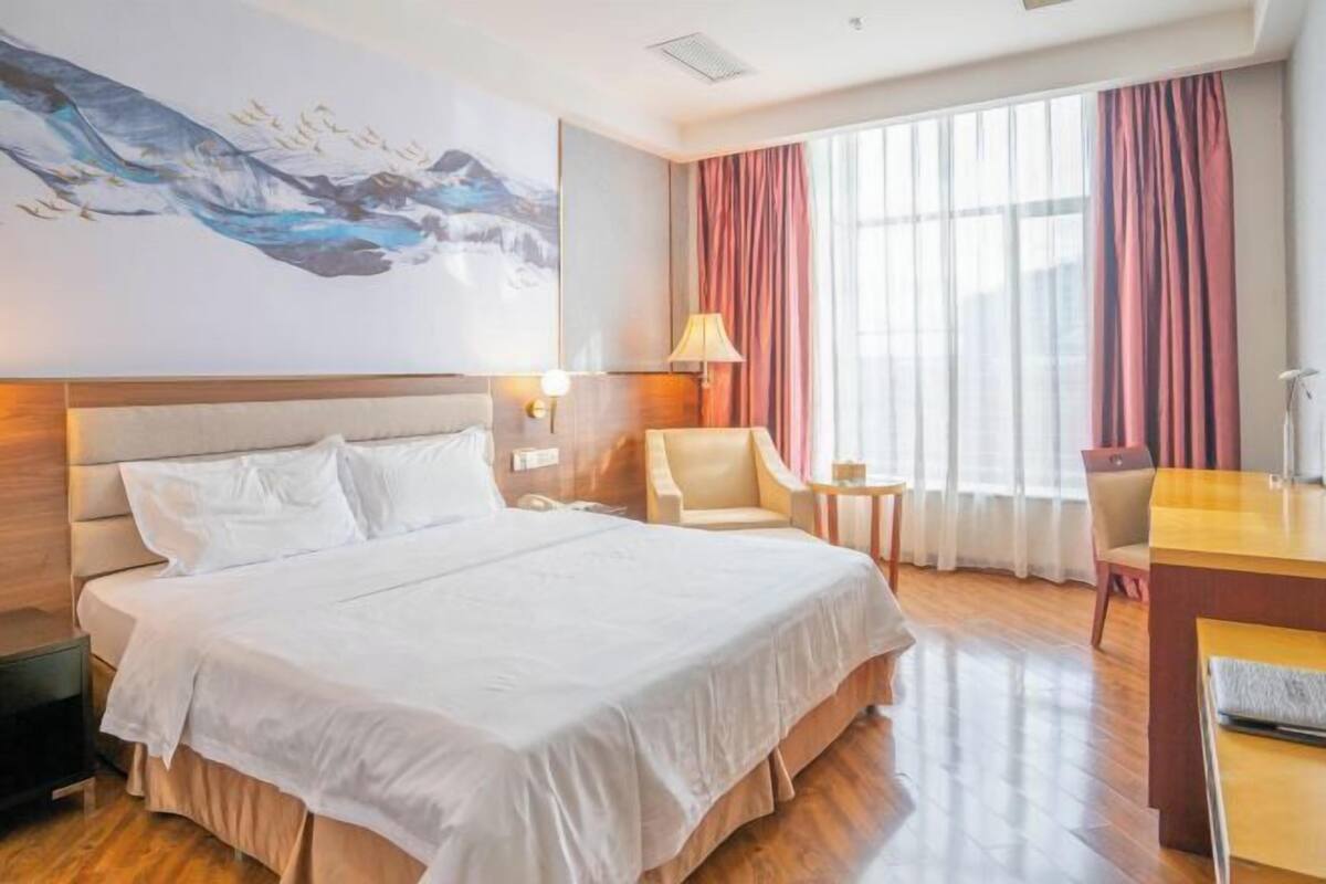 A hotel room with a large bed, a desk, a chair, a lamp, and a painting on the wall.
