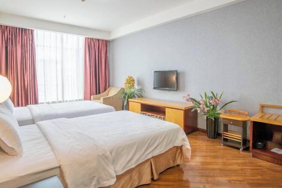 A hotel room with two beds, a desk, a television, and a window with curtains.