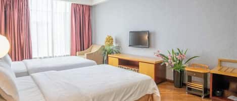 A hotel room with two beds, a desk, a television, and a window with curtains.