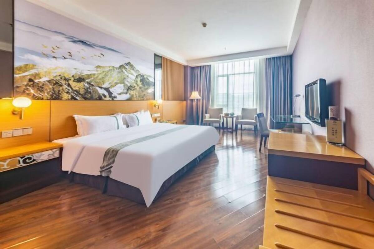 A hotel room with a bed, bedside tables, a desk, a chair, a television, and a large painting on the wall.
