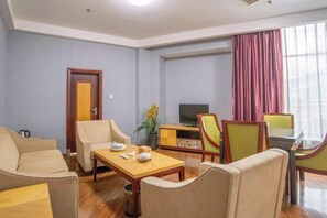 A hotel room with a sofa set, a dining table, a TV, and a window with curtains.