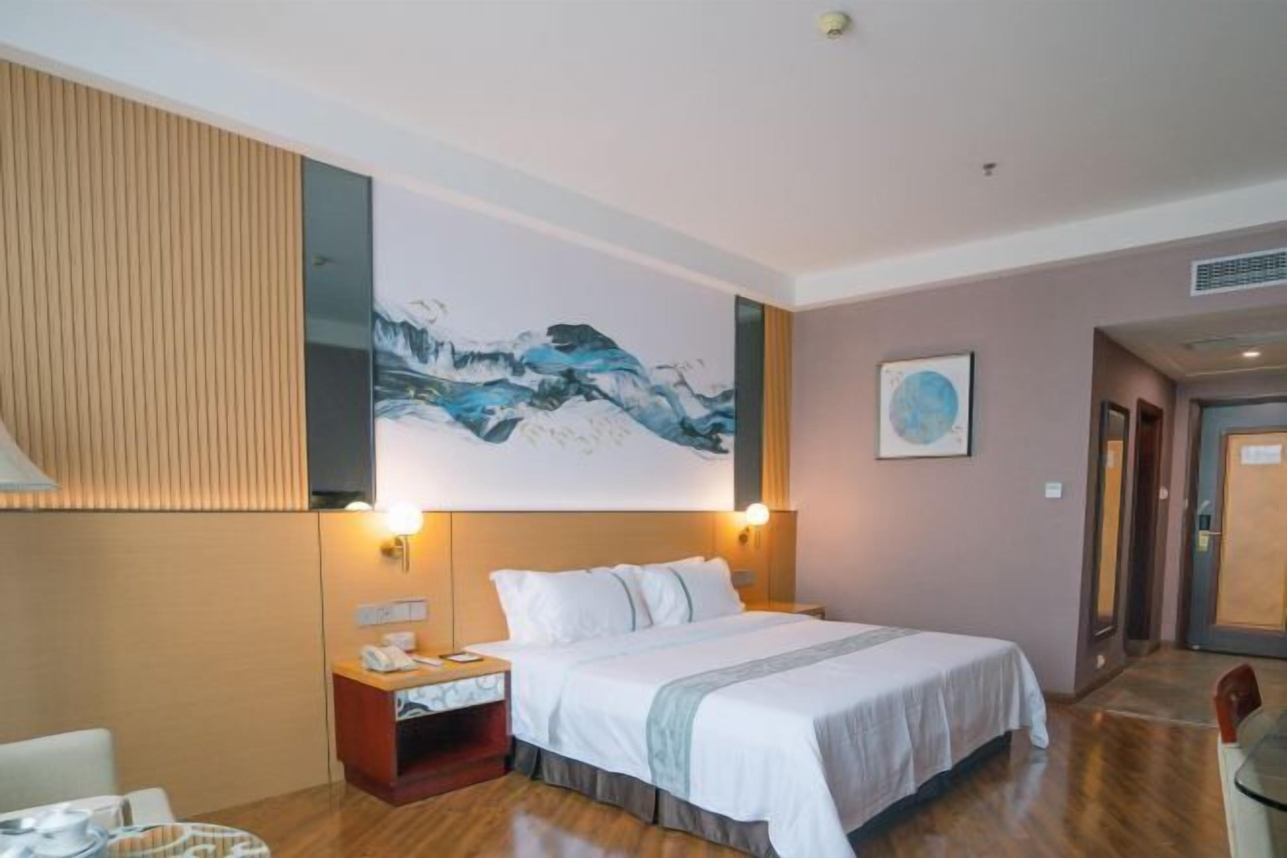 Una habitación de hotel con cama, mesita de noche, lámpara y una obra de arte en la pared.