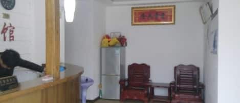 A reception area with a wooden desk, a chair, a refrigerator, and a wall-mounted clock.