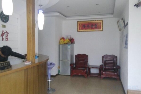 A reception area with a wooden desk, a chair, a refrigerator, and a wall-mounted clock. - Longyuan Express Hotel (Shanghai)