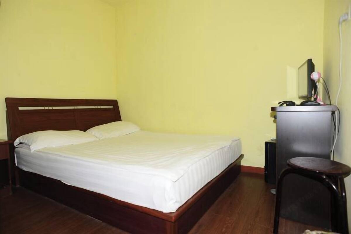A single bed with a wooden headboard in a room with yellow walls and wooden flooring.