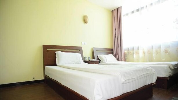 A hotel room with two single beds, wooden headboards, white linens, a nightstand, and a wall-mounted lamp. - Longyuan Express Hotel (Shanghai)