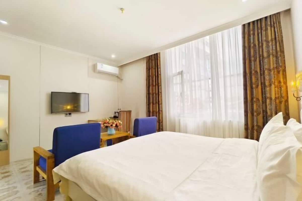 A hotel room with a bed, a desk, a chair, a TV, and a window with curtains.