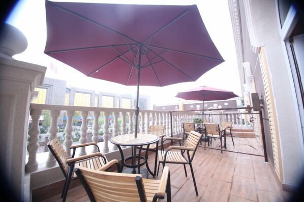 A balcony with wooden chairs and tables, a large umbrella, and a railing.