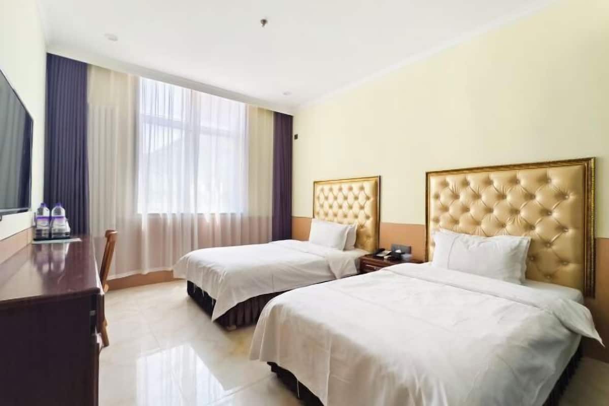 A hotel room with two beds, a desk, and a window with curtains.