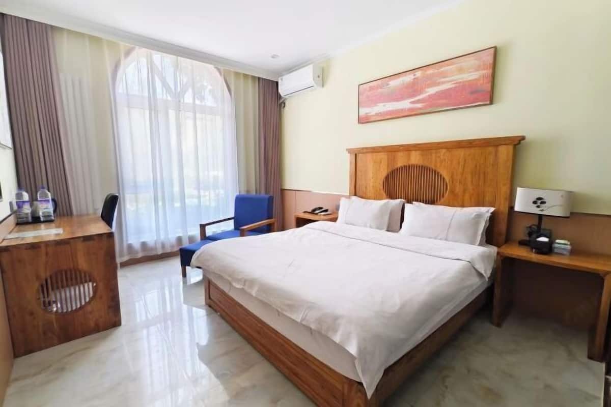 A hotel room with a large bed, a desk, a chair, a nightstand, and a window with curtains.