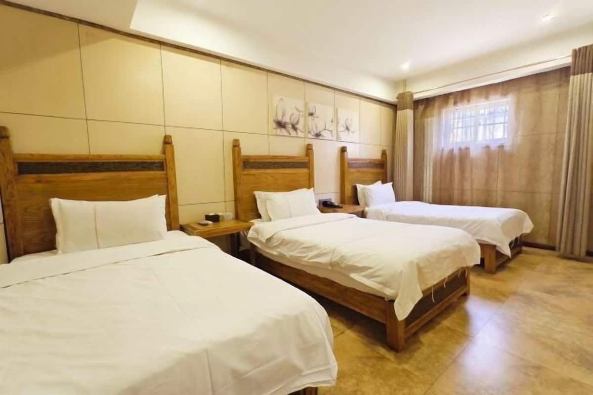 A hotel room with three wooden beds, a tiled wall with artwork, and a window with curtains.