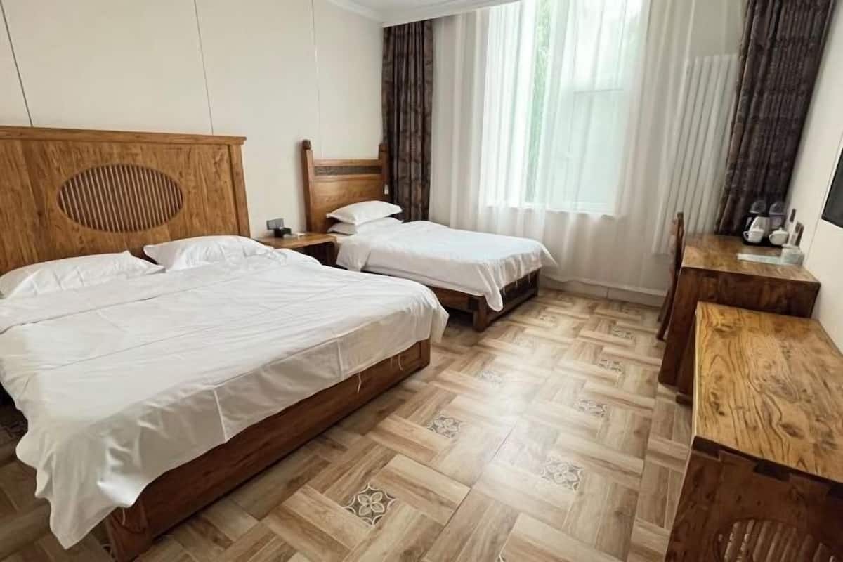 A hotel room with two beds, a wooden headboard, a nightstand, a wooden desk, and a window with curtains.