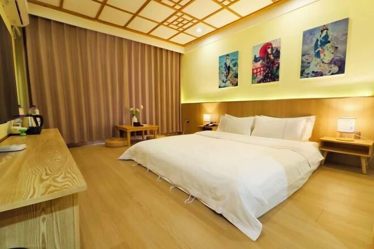 A hotel room with a wooden bed, a desk, a nightstand, and a large window with curtains.