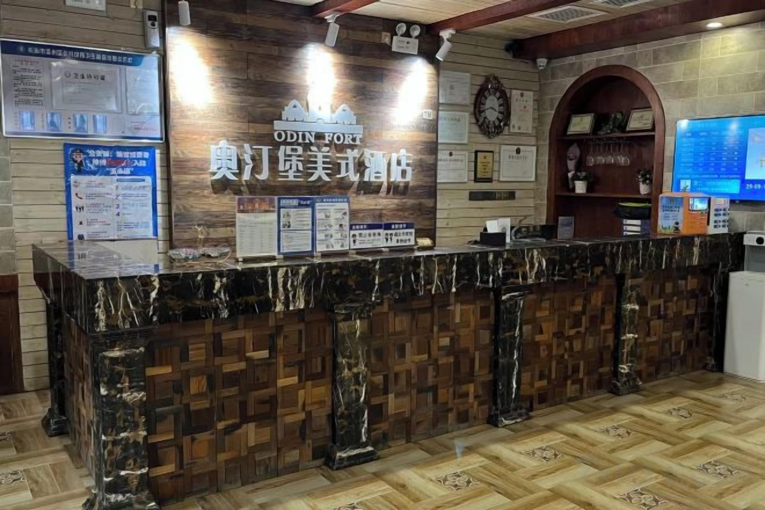 A hotel reception area with a marble counter, wooden paneling, and a digital screen displaying information.