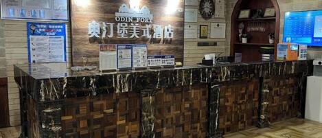 A hotel reception area with a marble counter, wooden paneling, and a digital screen displaying information.