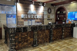 Zona de recepción de un hotel con mostrador de mármol, paneles de madera y una pantalla digital que muestra información.