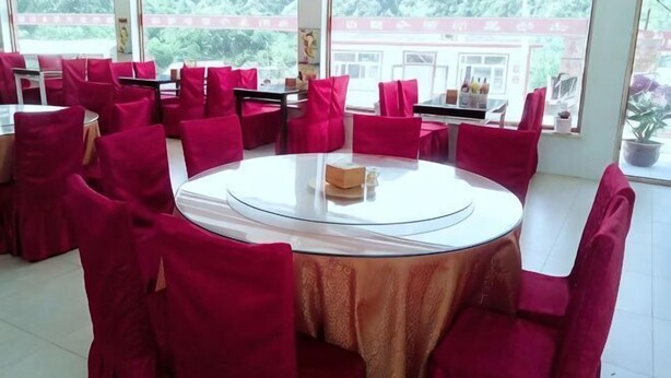 A dining area with round tables and red chairs, large windows with a view of greenery, and a white tablecloth on one table. - Bingyugou Jiahua Business Hotel (Zhuanghe)