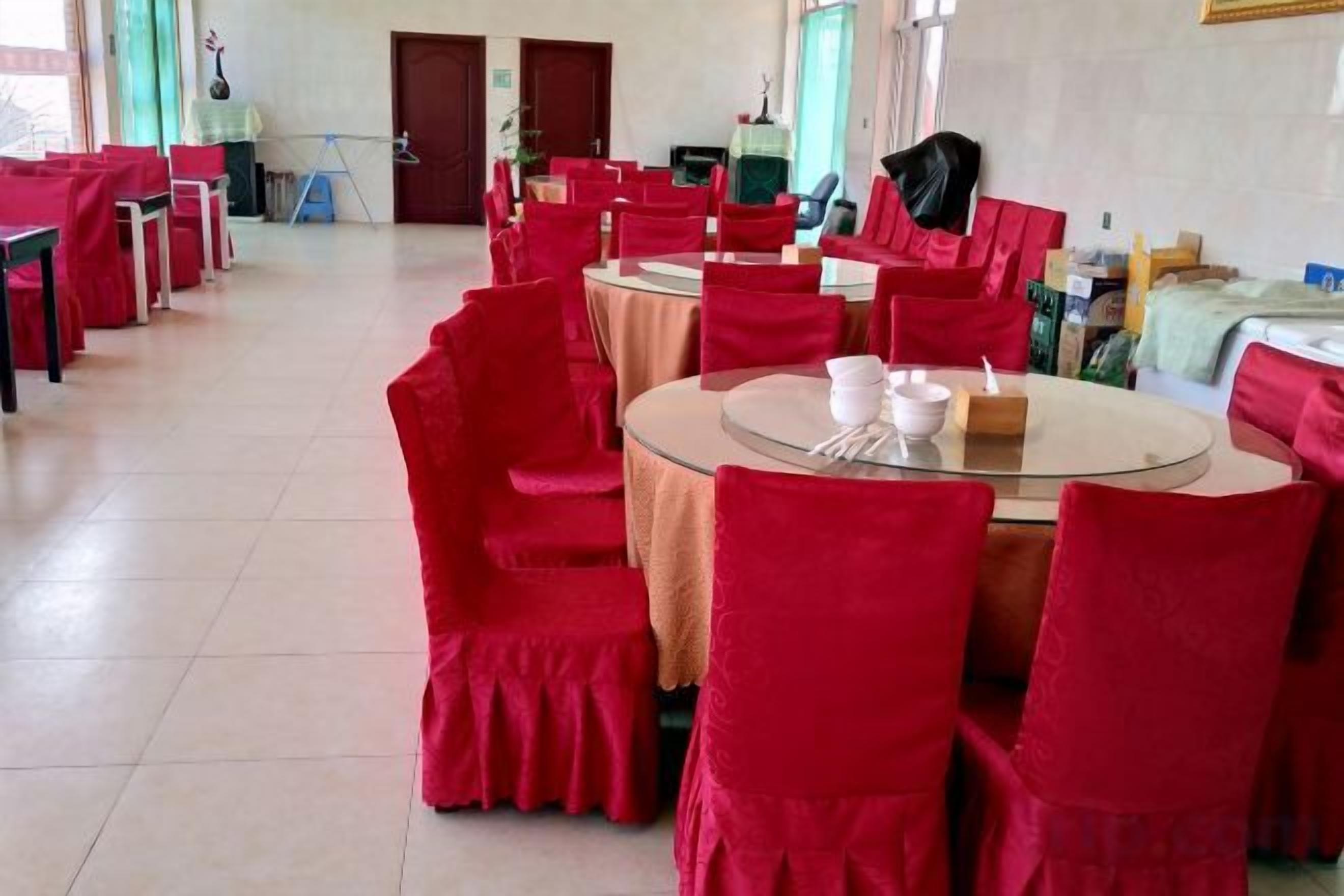 A dining area with round tables and red chairs, some tables have white tablecloths.