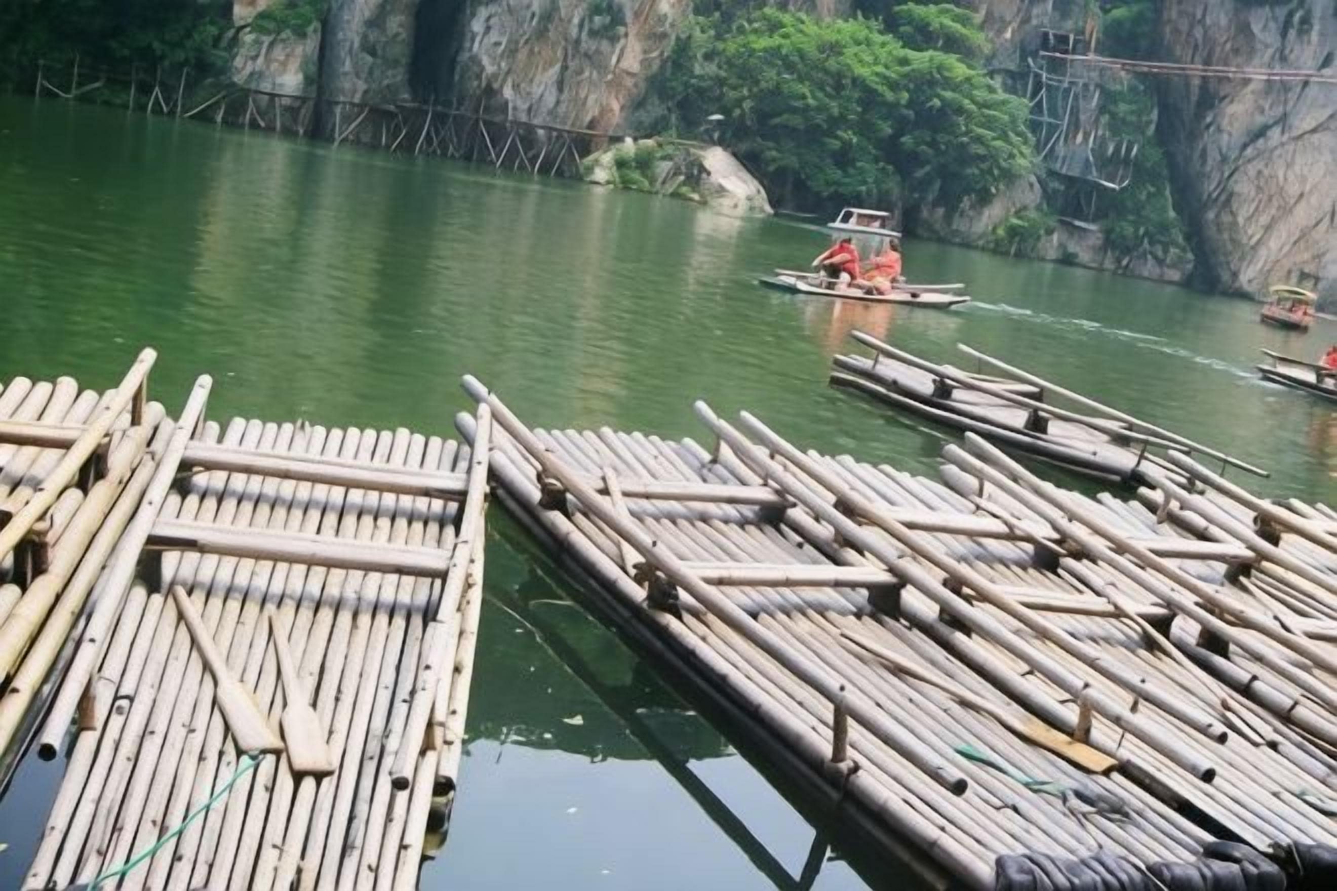 A bamboo raft docked at a riverbank with a rocky cliff in the background.