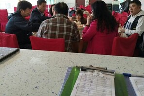 A dining area with red chairs and tables, a laptop on the table, and a clipboard with papers. - Bingyugou Jiahua Business Hotel (Zhuanghe)