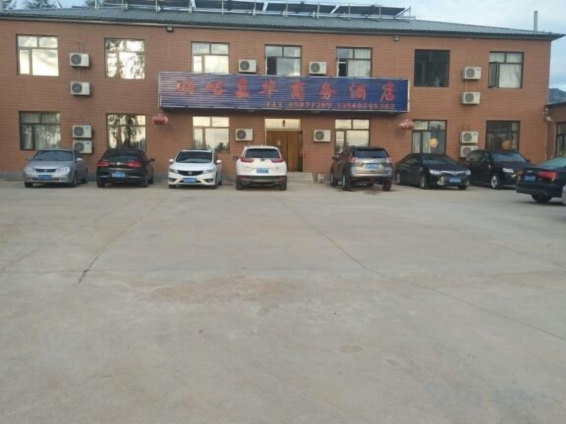 A building with a sign, multiple parked cars, and air conditioning units.