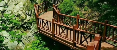 A wooden bridge with railings over a rocky stream, surrounded by lush greenery.