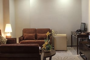 A living room with a sofa, a small table with a vase, a lamp, and a desk with a computer. - Qingtengyuan Hotel (Binzhou)