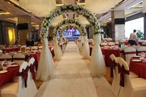 Une salle de banquet avec des tables disposées en rangées, une allée centrale et une arche décorée de fleurs.