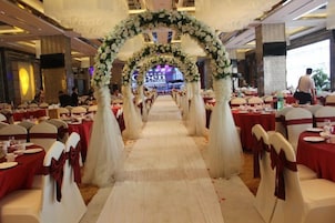 A banquet hall with tables arranged in rows, a central aisle, and a floral archway.