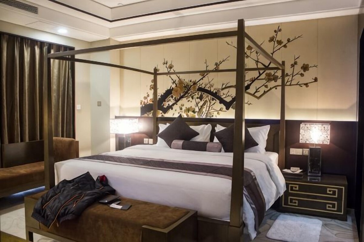 A four-poster bed with a canopy, a bedside table, a lamp, and a decorative wall piece.