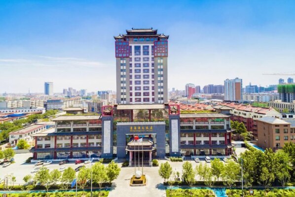 A multi-story hotel with a traditional architectural style, featuring a central entrance with a decorative roof, surrounded by a landscaped courtyard.
