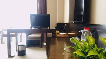 A hotel room with a television, a desk, a chair, a plant, and a bottle of water.