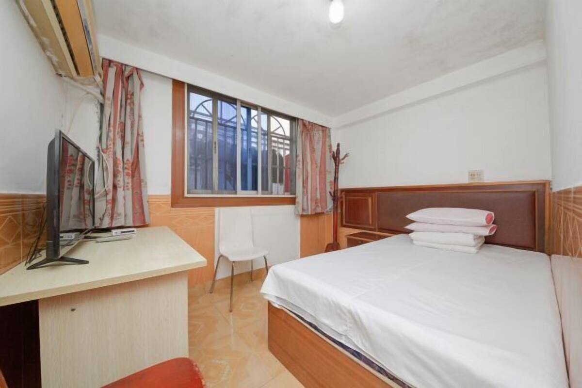 A bedroom with a bed, a desk, a chair, and a window with curtains.