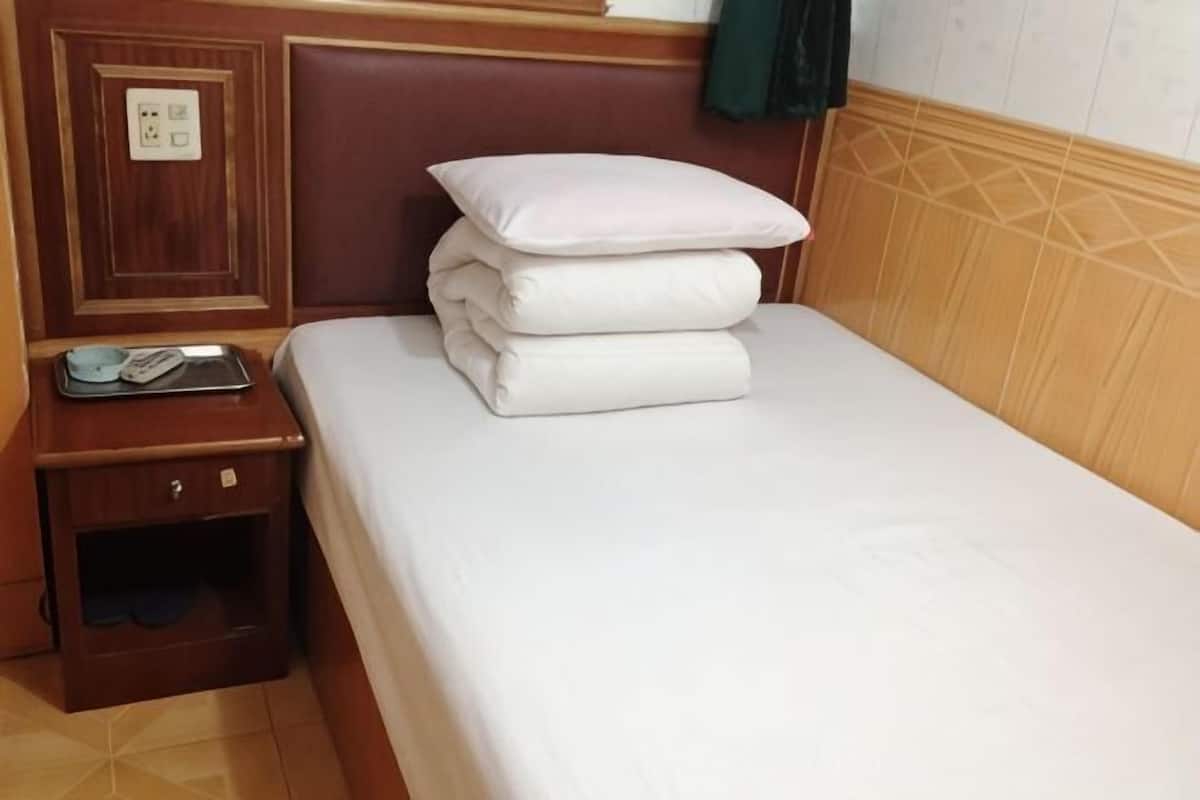 A neatly made bed with pillows, a bedside table with a phone and a tray, and a power outlet on the wall.