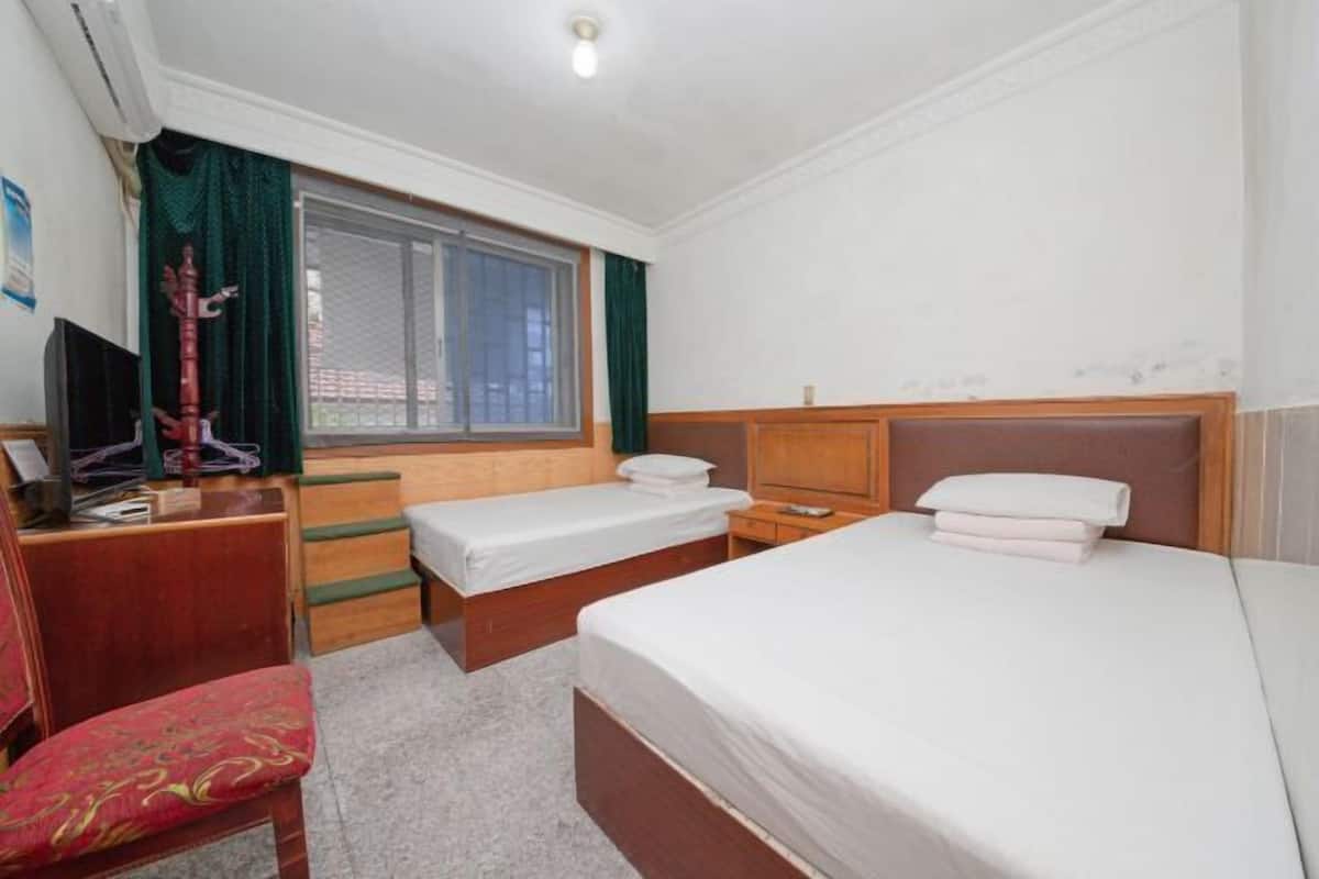 A hotel room with two single beds, a desk with a chair, a TV, and a window with curtains.