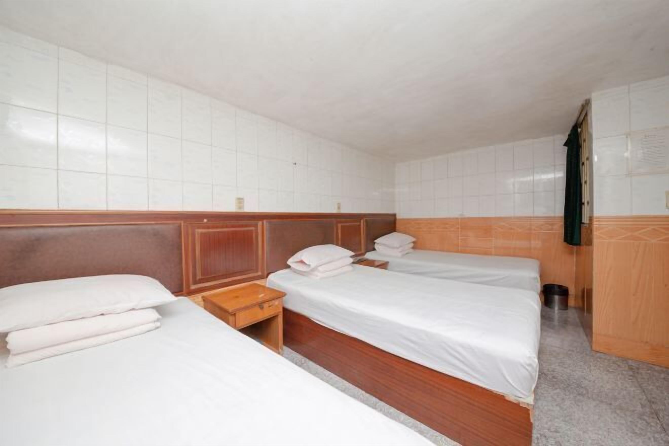 Una habitación de hotel con tres camas individuales, cabeceros de madera y una pared con azulejos.