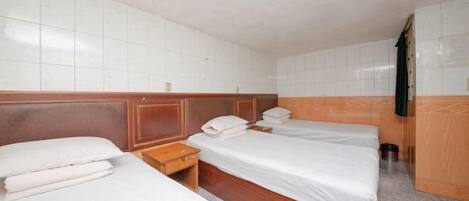 Una habitación de hotel con tres camas individuales, cabeceros de madera y una pared con azulejos.