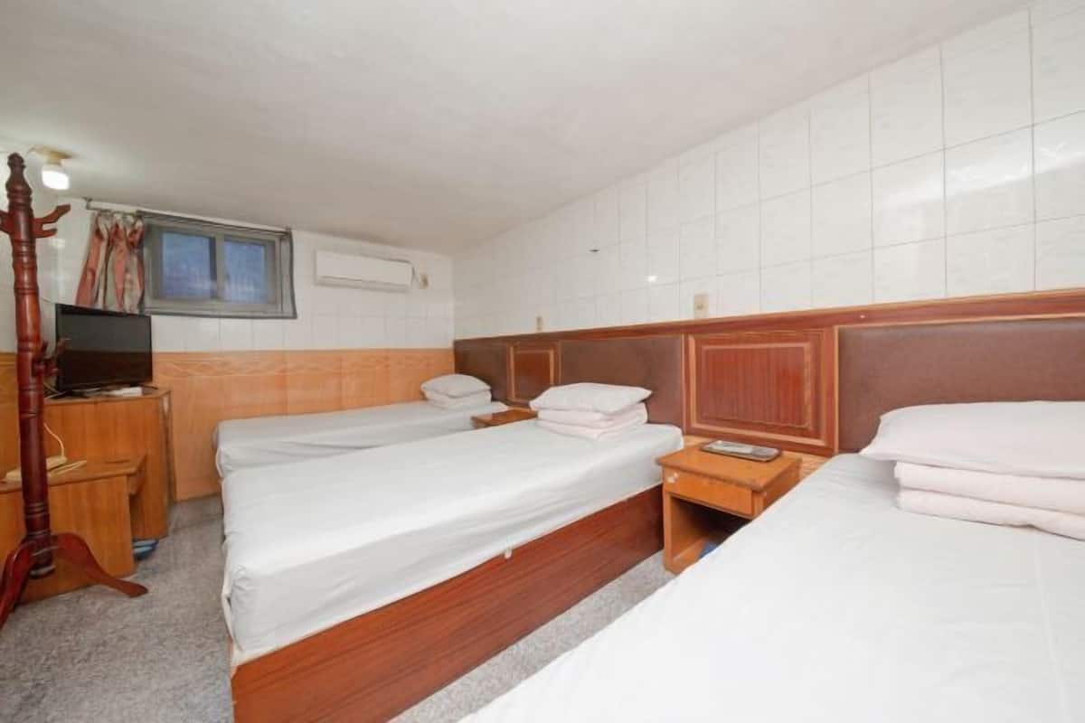 A hotel room with two beds, wooden headboards, a television on a wooden stand, and a window with curtains.