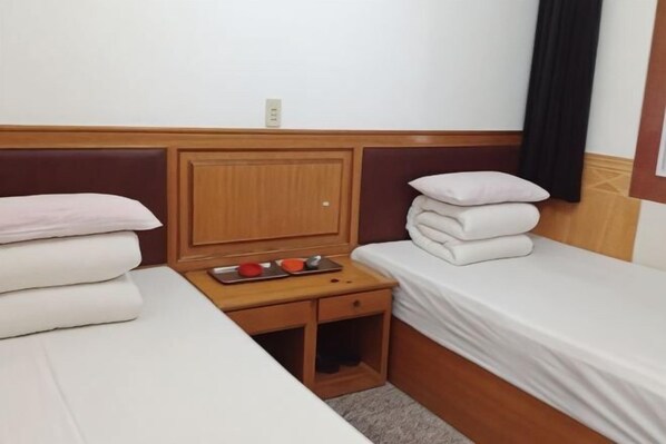 Une chambre d’hôtel avec deux lits, une tête de lit en bois, une petite table de chevet en bois avec un plateau, et une prise électrique au mur.
