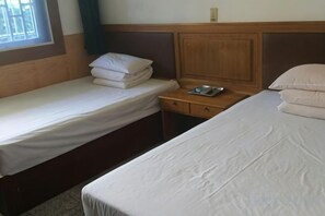 Une chambre d’hôtel avec deux lits simples, une tête de lit en bois, une table de chevet avec un plateau, et une fenêtre avec des rideaux.