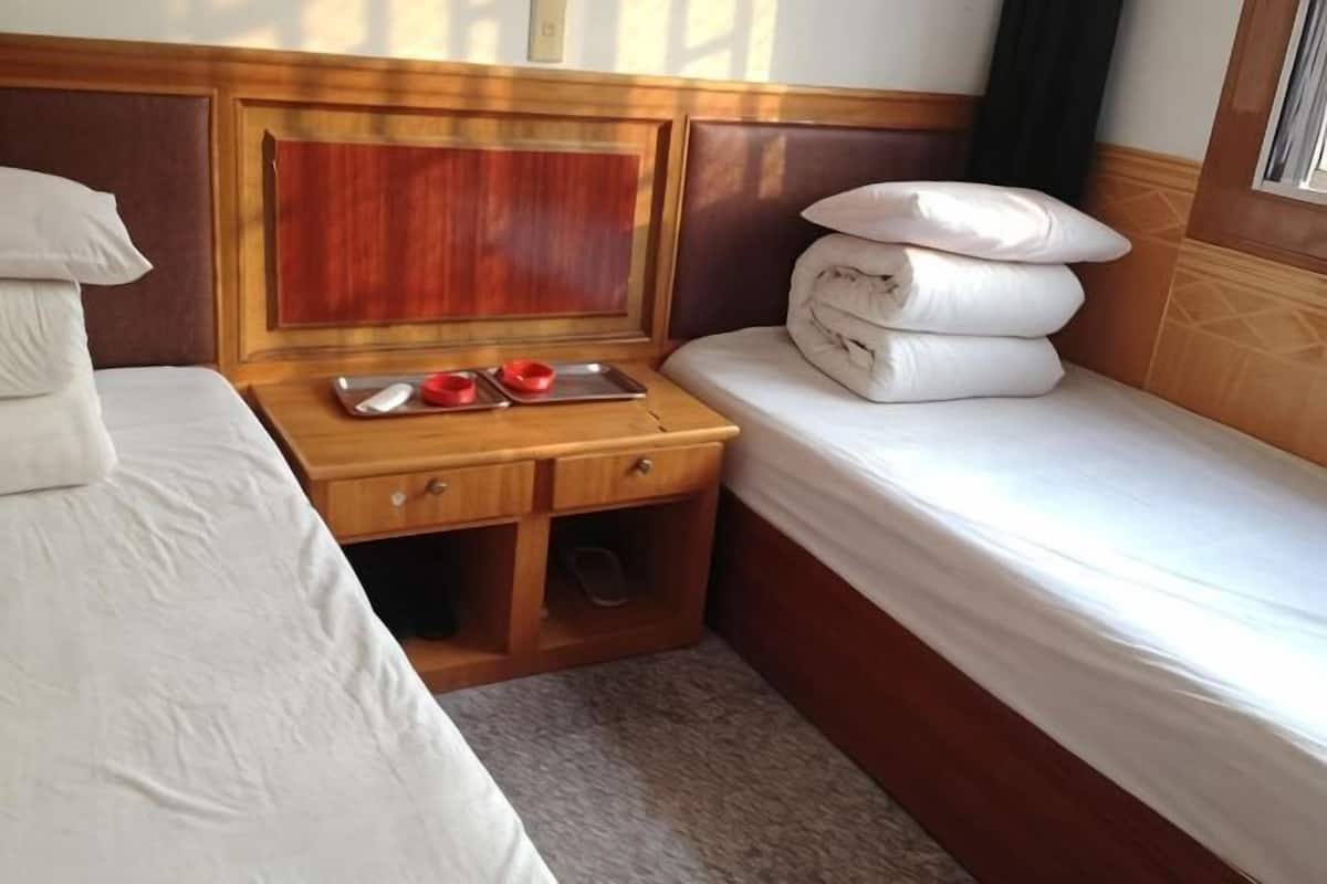 A hotel room with a bed, a wooden nightstand, a small shelf, and a window.