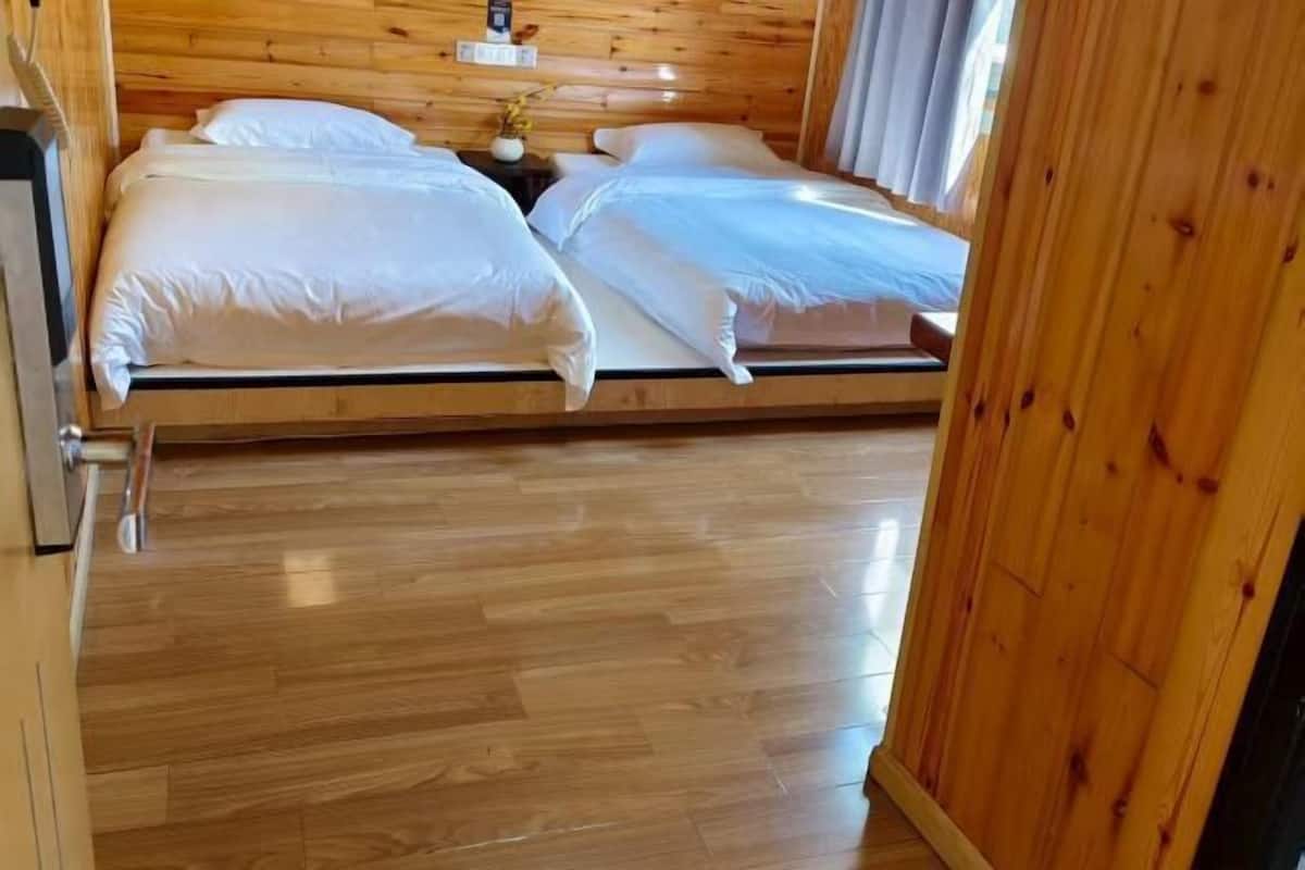 Une pièce aux murs lambrissés, avec deux lits, un plancher en bois et une petite table sur laquelle est posé un vase.