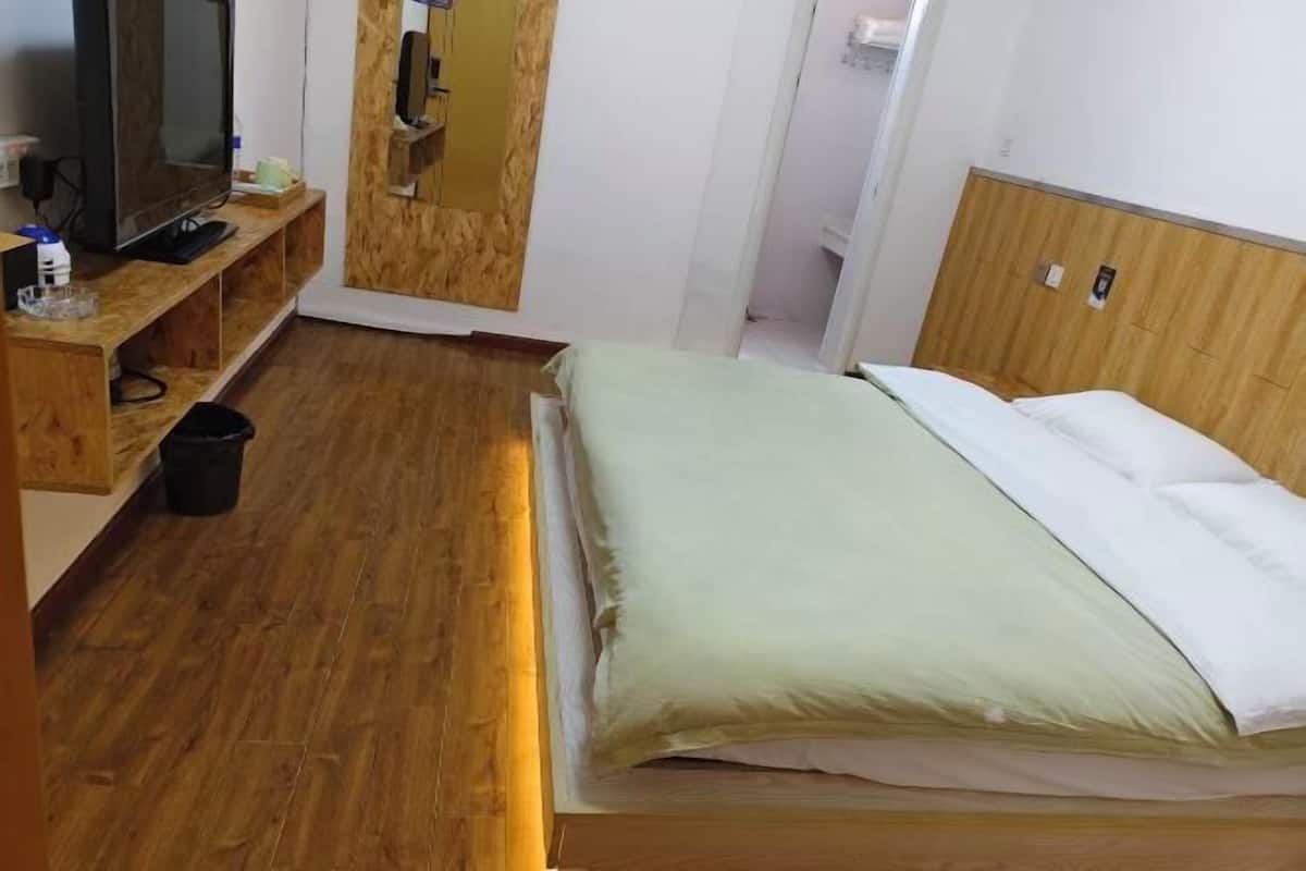 Une pièce comprenant un lit, un meuble en bois pour la télévision et une poubelle.