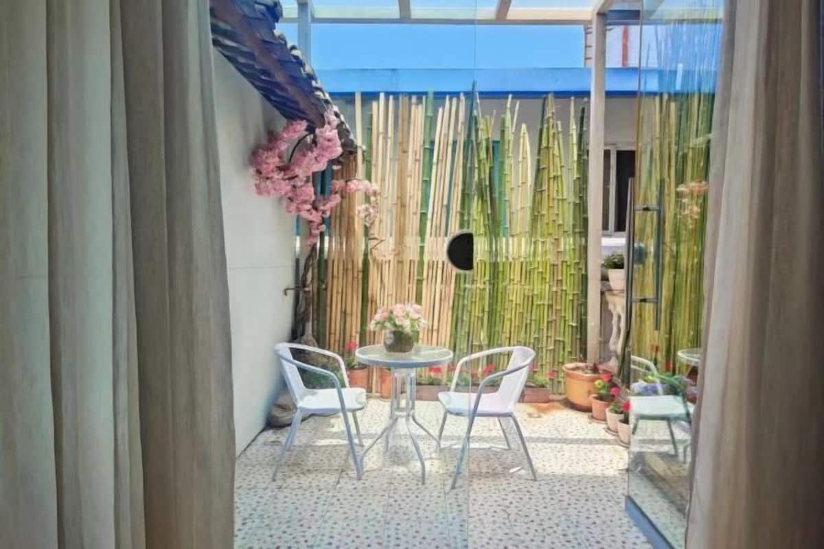 Une petite terrasse avec une table ronde et deux chaises, entourée de plantes de bambou et d’une clôture en bambou.